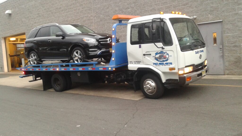 A tow truck carrying a black car on its flatbed, parked on the side of the road.