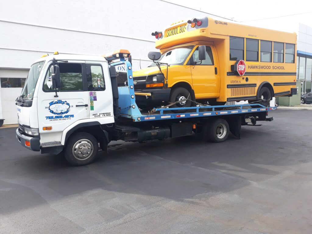 A tow truck carrying a yellow school bus on its flatbed, parked on the side of the road.